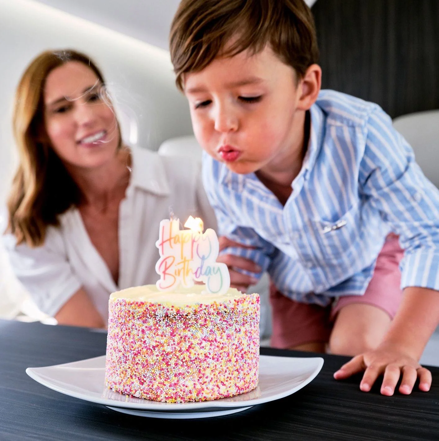 Child blowing out candles of birthday cake while flying on private jet